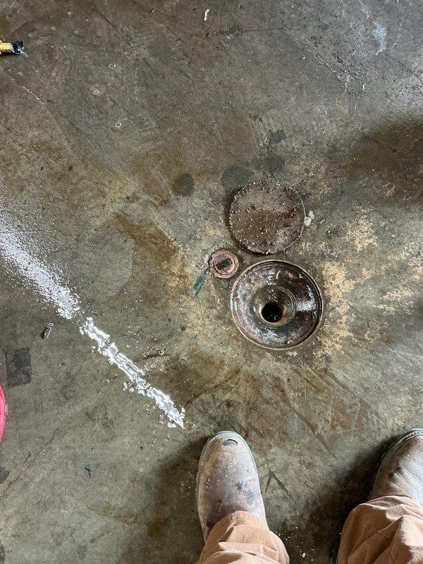 Responded to commercial retail facility for clogged floor drain in receiving room with standing water creating safety hazard near entrance. Upon arrival, found floor drain backing up with stagnant water pooling on concrete surface. Removed drain grate and caps to inspect drain assembly, documented extensive water damage and staining on surrounding floor area, and assessed blockage severity in main drain line.
