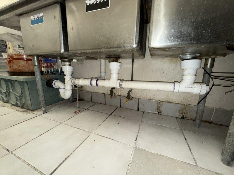 Responded to service call for multiple leak points in commercial kitchen drain system. Upon inspection, identified several compromised connections in the three-basin stainless steel sink assembly where PVC P-traps connected to the main horizontal waste line. Tightened slip joint connections at each trap, replaced deteriorated washers and compression seals that had failed due to age and thermal stress from commercial use. Verified proper drainage flow through all three basins and confirmed all leak points were eliminated. Tested system under full operational pressure to ensure watertight connections throughout the drain assembly.