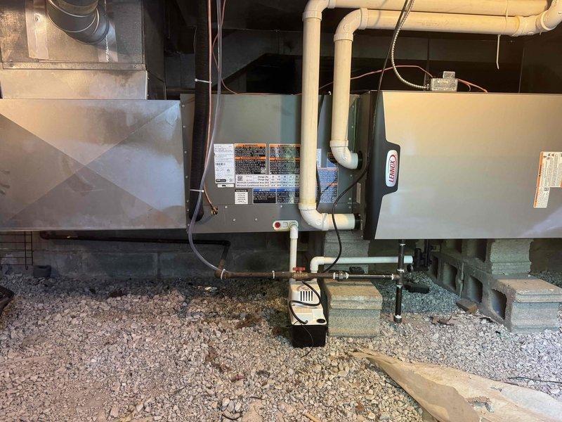 Completed full HVAC system installation including Lennox gas furnace and air conditioning unit with ductwork modifications. Installed air handler unit in basement utility area with proper mounting and leveling, connected white PVC condensate drain lines with appropriate vertical and horizontal runs, and integrated condensate pump for drainage management. Positioned outdoor AC condenser unit on concrete pad with gravel base for proper drainage and vibration isolation. Ran refrigerant line sets between indoor and outdoor equipment with proper insulation and securing. Modified existing ductwork with flexible silver duct connections to air handler, ensuring proper airflow distribution throughout the system. Completed all electrical connections including power supply conduits, control wiring between components, and safety disconnect installation. Installed all required safety labels and manufacturer specifications on equipment. Secured all piping, wiring, and ductwork to structural framing 