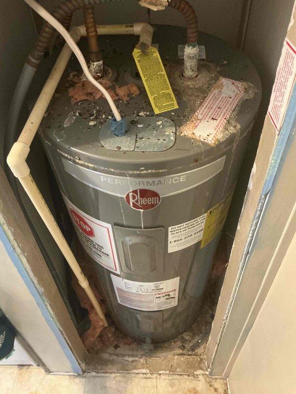 Conducted on-site evaluation of residential Rheem Performance water heater showing significant age-related deterioration. Documented extensive corrosion and mineral deposits on top of tank, corroded copper piping connections, and weathered flexible supply lines requiring replacement to prevent potential failure and water damage.