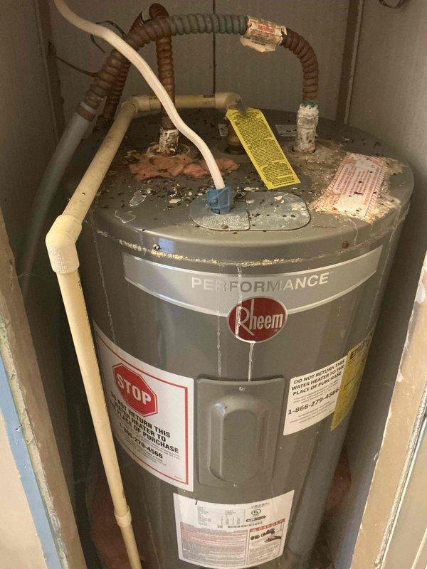 Conducted on-site evaluation of residential Rheem Performance water heater showing significant age-related deterioration. Documented extensive corrosion and mineral deposits on top of tank, corroded copper piping connections, and weathered flexible supply lines requiring replacement to prevent potential failure and water damage.