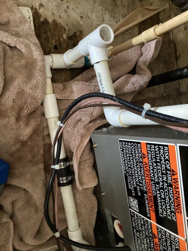 Responded to emergency no-cooling call for 1.5-year-old Lennox ML14KC1 system that had been previously shut down by fire department due to burning plastic smell. Upon arrival, confirmed clogged condensate drain line causing water leakage. Cleared drain line obstruction and verified proper drainage flow through PVC condensate system. Inspected all electrical connections and components for signs of overheating or damage related to previous burning smell complaint. Tested system operation and confirmed unit cooling properly with no unusual odors detected. Documented drain line configuration and connections with photos for service records.