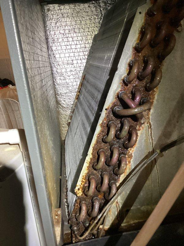 # HVAC Service Report - A/C System Leak Investigation

Responded to service call for reported system leak. Upon arrival, performed comprehensive inspection of air conditioning system, with particular focus on areas previously serviced for leakage issues.

Conducted thorough examination of air handler unit, accessing interior components through top cabinet panels. Inspection revealed significant accumulation of dust and debris within unit, indicating potential moisture intrusion. Noted evidence of previous leak activity with visible rust-colored particles and staining on metal base surfaces.

Proceeded with detailed assessment of evaporator coil assembly and surrounding refrigerant lines. Discovered extensive corrosion and oxidation on copper refrigerant coils, with heavy brownish-orange rust buildup concentrated along coil bends and joints. Corrosion pattern consistent with prolonged moisture exposure and indicates advanced deterioration of coil integrity.

Documented findings with pho
