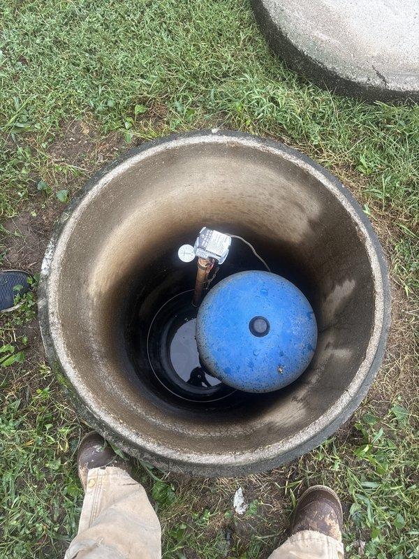 Responded to emergency call for reported cracked pipe with active water leak at residential property. Upon arrival and inspection, determined the issue was related to the well system rather than a burst pipe. Assessed the concrete well vault and blue pressure tank assembly, inspecting all visible components, connections, and fittings for signs of water intrusion or system failure. Confirmed main water valve had been shut off as precaution. Documented well system condition with photographs showing pressure tank, pump components, and vault interior for diagnostic purposes and future reference.