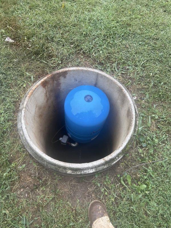 Responded to emergency call for reported cracked pipe with active water leak at residential property. Upon arrival and inspection, determined the issue was related to the well system rather than a burst pipe. Assessed the concrete well vault and blue pressure tank assembly, inspecting all visible components, connections, and fittings for signs of water intrusion or system failure. Confirmed main water valve had been shut off as precaution. Documented well system condition with photographs showing pressure tank, pump components, and vault interior for diagnostic purposes and future reference.