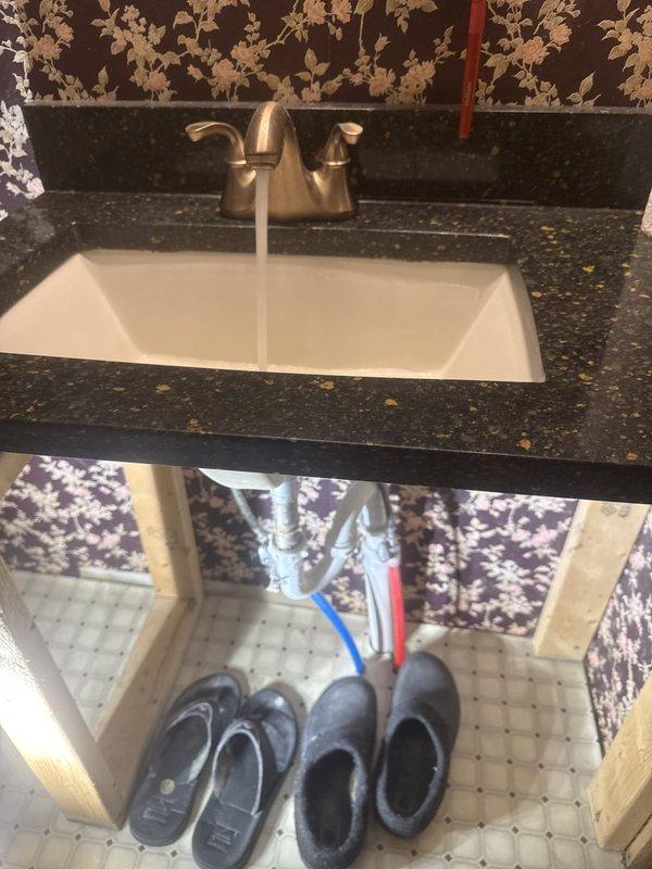 Completed monthly plumbing inspection of residential property, examining bathroom vanity plumbing connections and water heater system. Verified proper operation of undermount sink faucet, inspected P-trap and hot/cold water supply lines for leaks or deterioration, and documented Navien NPE-210A tankless water heater in good working condition with all components functioning within normal parameters.