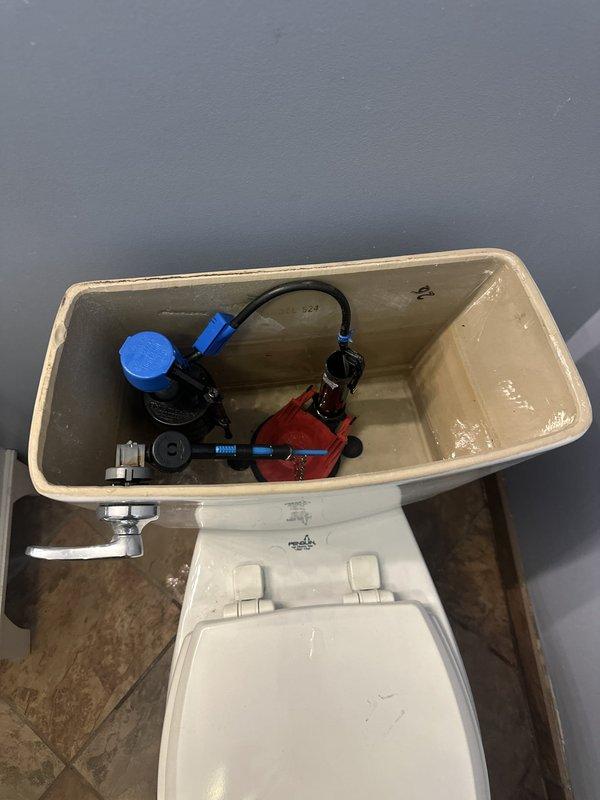 Responded to residential service call for toilet tank repair. Upon inspection, found aging flush valve assembly and fill valve mechanism with visible mineral deposits and hard water buildup throughout tank interior. Removed and replaced complete internal tank components including fill valve assembly, flush valve, flapper, and connecting hardware. Installed new blue-capped fill valve with refill tube and new flush valve system. Adjusted water level to manufacturer specifications and tested flush cycle for proper operation. Verified all connections were secure and leak-free before completing service.
