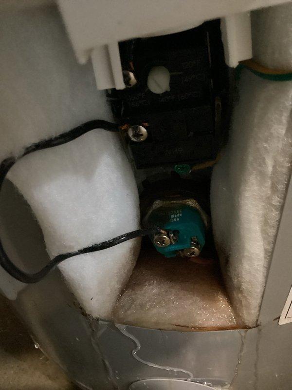 Responded to water leak complaint originating from garage area. Upon inspection, identified moisture accumulation at base of utility enclosure containing electrical components and plumbing connections. Examined water heater installation in unfinished space with exposed wooden framing and found multiple plumbing connections including hot and cold water supply lines with red and blue handles, flexible braided stainless steel connectors, and copper piping with various fittings and valves. Documented conditions with photographs showing electrical relay components, turquoise terminal blocks, and white foam insulation material around connections. Noted visible water or moisture accumulation on floor surface beneath utility enclosure. Assessed HVAC ductwork, water heater mounting, and all associated plumbing connections to determine source of leak. Investigation revealed potential leak point near water heater plumbing assembly requiring further monitoring or repair.