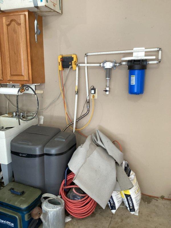 Responded to service call regarding excessive lime buildup on water heater system. Upon arrival, conducted thorough inspection of the tanked water heater and surrounding plumbing infrastructure. Documented existing conditions including water treatment equipment, filtration system with blue canister filter, water softener unit, and associated PVC piping and gas lines. Assessed lime scale accumulation on water heater components and evaluated overall system performance. Provided customer with recommendations for descaling treatment options and discussed maintenance procedures to prevent future mineral buildup. Photographed installation for service records.