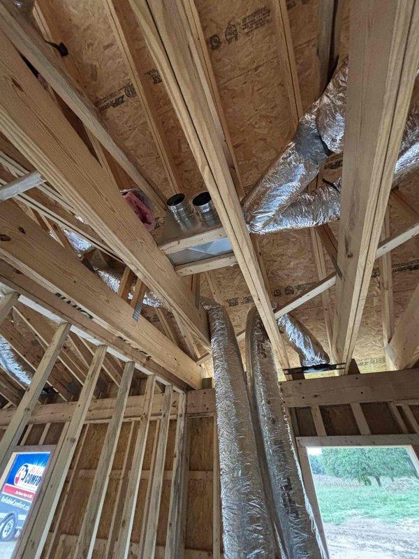 Commenced HVAC rough-in installation for new residential construction, successfully routing flexible ductwork through exposed ceiling joists and roof framing structure. Initial ductwork runs were installed and secured with proper support brackets, establishing the foundation for the complete HVAC distribution system throughout the building envelope.