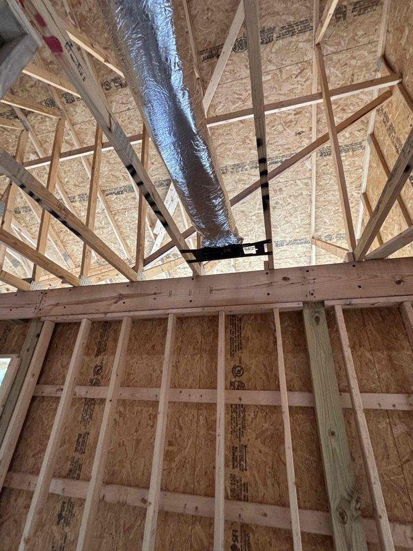 Commenced HVAC rough-in installation for new residential construction, successfully routing flexible ductwork through exposed ceiling joists and roof framing structure. Initial ductwork runs were installed and secured with proper support brackets, establishing the foundation for the complete HVAC distribution system throughout the building envelope.