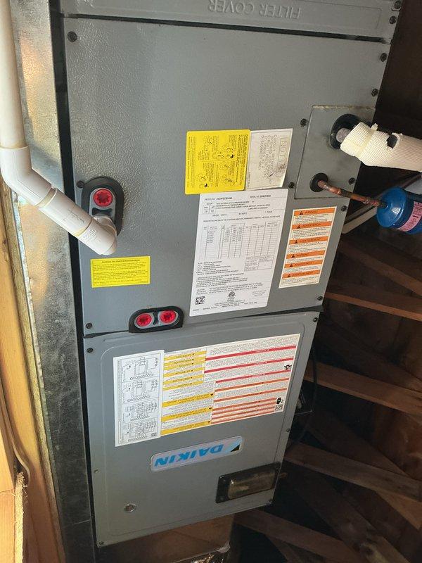 Completed basic monthly heating maintenance on Daikin CCHP system located in basement/utility area with attic access required via ladder. Performed standard inspection of air handler unit including visual examination of evaporator coil fins, heat exchanger components, and refrigerant line connections, verifying all components were clean and operational. Documented system condition through photographs showing unit labels, safety information, and interior coil assembly in satisfactory working order.