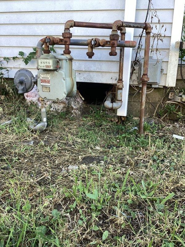 Responded to customer complaint regarding inadequate heating performance during previous winter season despite thermostat set to 90°F. Performed crawlspace inspection to assess ductwork condition and identify heat loss issues. Accessed difficult crawlspace area with limited clearance and navigated through debris and challenging conditions. Documented extensive deterioration of crawlspace insulation, including damaged and detached foil-backed vapor barrier material on foundation walls. Observed exposed floor joists with moisture staining and discoloration indicating potential air infiltration pathways. Identified compromised building envelope allowing conditioned air loss and reducing system efficiency. Placed ventilation fan in crawlspace for air circulation and moisture management. Photographed existing conditions including deteriorated insulation, damaged vapor barrier, exposed soil floor, and aged exterior gas meter installation with corroded piping. Recommended comprehensive ductwo