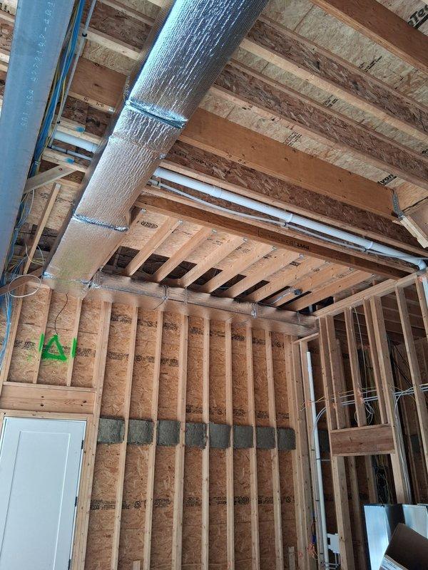 Completed three-day HVAC ducting rough-in at residential new construction site. Installed large-diameter supply trunk line with reflective insulation wrap, secured with proper strapping at code-compliant intervals throughout exposed ceiling joists. Routed flexible ductwork and rectangular metal duct runs through framed structure, coordinating with electrical and other trades to ensure proper clearances and support.