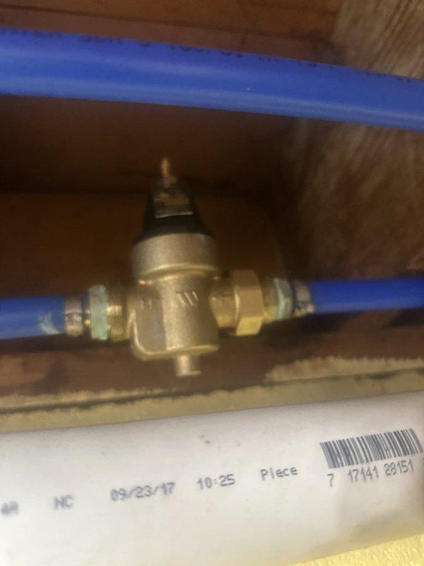 Returned to property to replace the pressure reducing valve on the main water supply line. Removed the existing PRV and installed a new brass pressure reducing valve with compression fittings on the blue PEX piping system. The valve was properly positioned and secured within the wooden framing cavity, with the adjustment mechanism accessible for future pressure adjustments. System was tested and confirmed to be operating within proper pressure parameters.