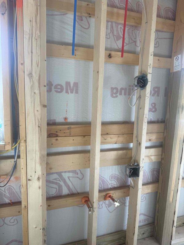 Conducted site visit to assess faucet installation in active construction environment. Documented rough-in plumbing configuration including hot and cold PEX supply lines, orange-handled shut-off valves, and fixture placement within framed wall cavity with reflective insulation. Verified protective measures in place and photographed current plumbing infrastructure for future fixture installation planning.
