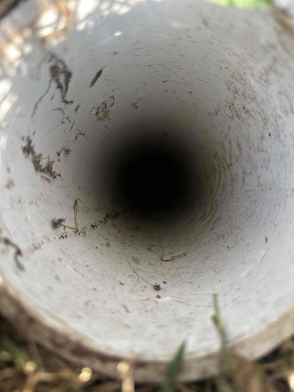 Responded to complaint of gurgling in bathroom sink and shower when toilet is flushed. Inspected main bathroom plumbing system and identified drainage ventilation issue. Located and examined roof vent pipe serving the bathroom plumbing fixtures. Found vent pipe partially obstructed with debris, organic matter, and accumulated dirt on interior walls, restricting proper air flow. Documented condition of vent pipe interior showing staining, contamination, and blockage contributing to negative pressure in drain system. The restricted vent was causing improper drainage venting, resulting in air being pulled through sink and shower drain traps when toilet discharged, creating the reported gurgling sounds. Photographed vent pipe condition for service records.