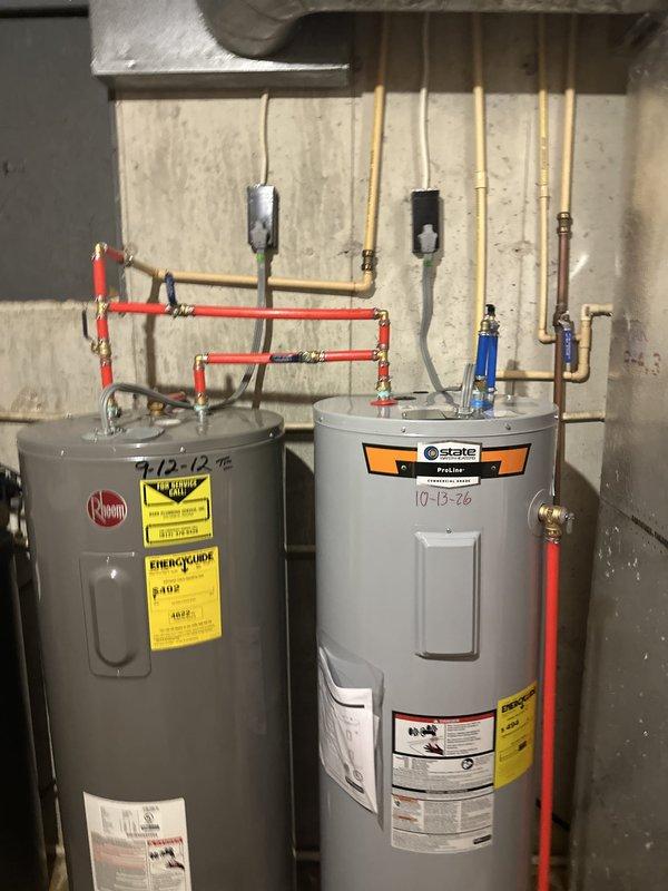 Performed an on-site estimate for replacement of a 50-gallon electric tank water heater (model LTA052KK), inspecting the existing Rheem unit alongside an adjacent State ProLine heater and their interconnecting supply piping, valves, and electrical connections. Documented unit labeling and piping configuration, noting damp concrete flooring around the tank bases with no active leaks observed, and discussed the customer's air conditioning concerns.