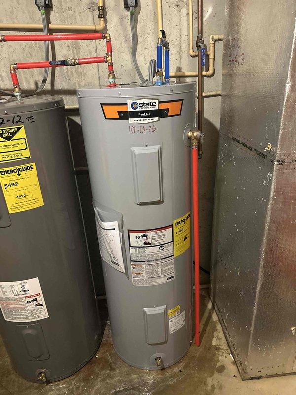 Performed an on-site estimate for replacement of a 50-gallon electric tank water heater (model LTA052KK), inspecting the existing Rheem unit alongside an adjacent State ProLine heater and their interconnecting supply piping, valves, and electrical connections. Documented unit labeling and piping configuration, noting damp concrete flooring around the tank bases with no active leaks observed, and discussed the customer's air conditioning concerns.