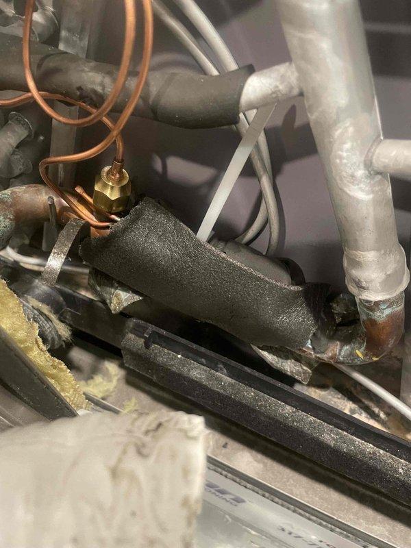 Replaced the failed thermostatic expansion valve (TXV) on the system, brazing in the new valve and reconnecting the refrigerant lines. Inspected the surrounding copper piping and found deteriorated, torn suction line insulation and oxidized solder joints, noting the need for proper re-insulation and monitoring. Verified ambient and system temperatures with a digital thermometer to confirm proper operation after the repair.
