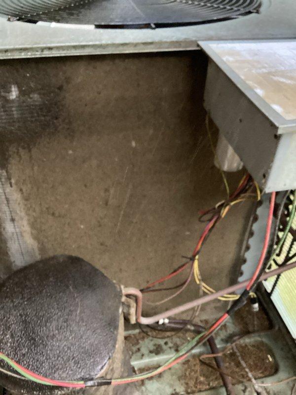 Performed seasonal tune-up on a 2013 model outdoor condensing unit, documenting unit data and condition. Inspection revealed heavy dust, lint, and debris matting on the condenser coil surface, along with leaves and debris on the cabinet floor, restricting airflow; coil and cabinet were cleaned to restore heat transfer. Noted weathered cabinet finish and an umbrella placed over the fan opening, which should be removed to prevent airflow obstruction and fan damage, and checked the electrical disconnect, wiring, and refrigerant line insulation.