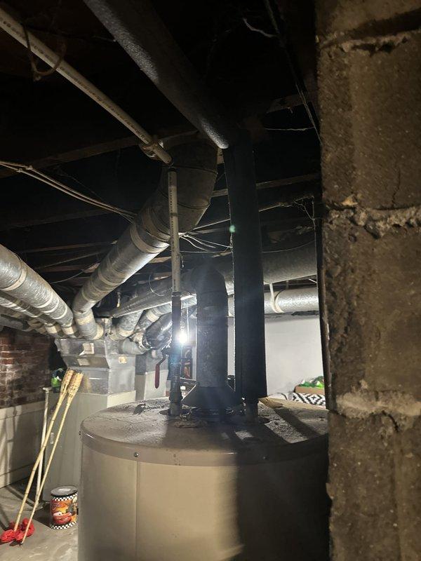 Assessed the existing tank-style water heater and its atmospheric flue venting in the basement mechanical area for conversion to a tankless unit. Evaluated available wall space, clearances, and the proximity of existing HVAC ductwork, supply piping, and electrical for proper installation, noting that venting, gas supply sizing, and combustion air requirements will need to be addressed. Documented the site conditions with photos to support the estimate for removal of the current unit and installation of the new tankless system.