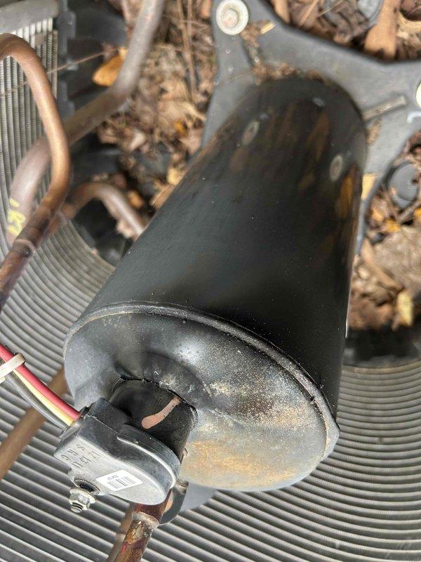 Responded to a no-cool complaint on a 5-year-old residential split-system condenser. Inspected the outdoor unit and found the compressor with surface rust and corrosion on the lower end cap, dirt and debris buildup on the housing, and leaf litter around the base. Verified the condenser fan and motor, evaluated the compressor and associated electrical connections and sensor wiring, and checked the refrigerant line set, noting tarnished copper tubing; findings indicate a possible compressor or refrigerant circuit issue contributing to the loss of cooling.