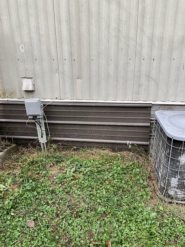 Performed an on-site evaluation for replacing an aging furnace with a heat pump system at a manufactured home, including assessment of the existing outdoor condenser, electrical disconnect, and exterior equipment placement. Documented the existing condenser, which showed dirty coil surfaces with mineral buildup, along with surrounding site conditions, to determine installation requirements and equipment sizing for the heat pump conversion.