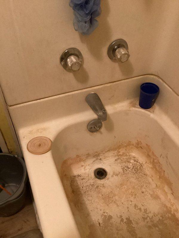Cleared a clogged bathtub drain by removing the stopper and clearing the blockage from the drain line, restoring proper flow. Verified unobstructed drainage by running water through the tub. Noted heavy rust staining and worn enamel on the tub basin.