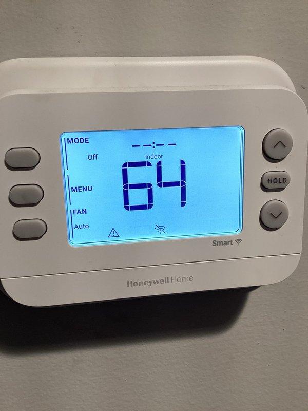 Performed A/C diagnostic evaluation on the system, confirming reported issues including a continuously running blower, a line set requiring reset, no emergency shut-off switch installed, and no filter present at the air handler. Inspected the Honeywell thermostat (displaying an alert with no Wi-Fi connectivity) and documented the air handler's condition, noting insulated suction line wear, rust staining at the line set penetration, and staining and moisture near the condensate drain piping. Findings were recorded with photos to support repair estimates, and a follow-up visit is recommended to quote corrective repairs.