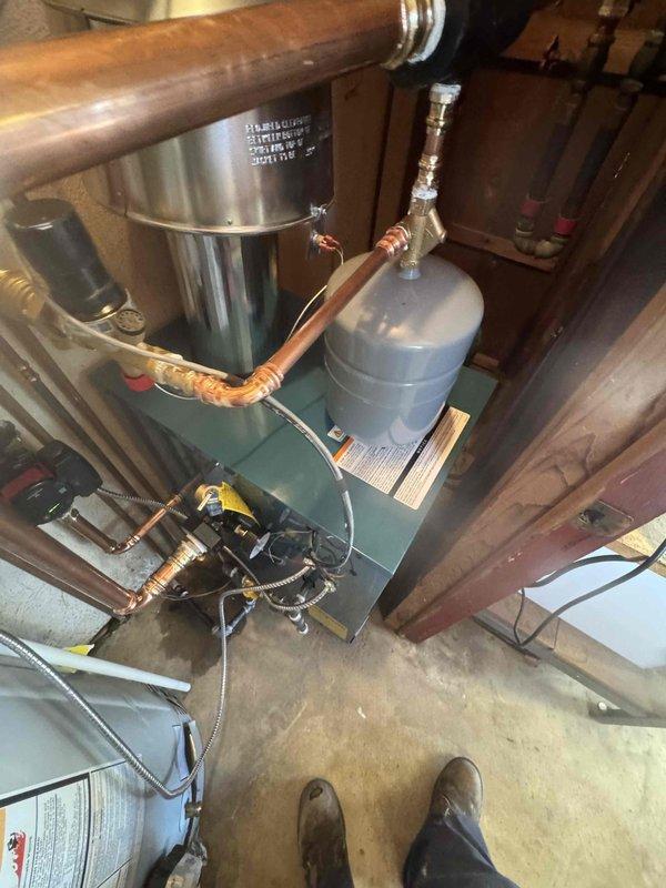 Installed a new boiler with an expansion tank mounted on top, connected via copper piping with a Y-strainer and brass fittings. Piped the system with soldered copper supply and return lines, a circulator pump, air separator, isolation valves, and a pressure gauge, and connected braided flexible lines and electrical wiring. Installed a stainless steel vent assembly and tied it into the existing flue stack alongside the gas water heater, with foil-taped joints sealed and warning labels in place.