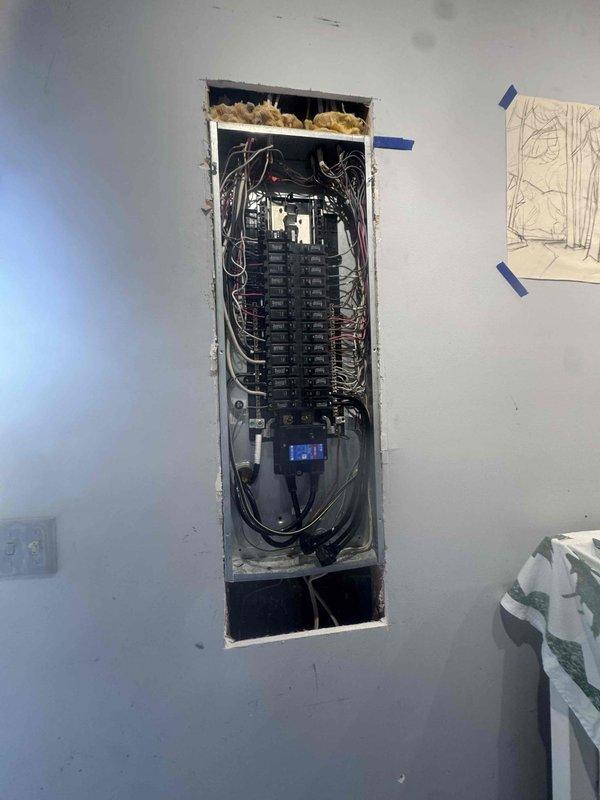 Responded to an install callback for a missing wire connection and a reported sewer odor at the water heater. Opened the drywall at the electrical panel, exposing the breaker box with the cover removed, to access and add the required wiring at the panel. Water heater odor complaint was documented for follow-up evaluation, including drain trap and venting inspection.