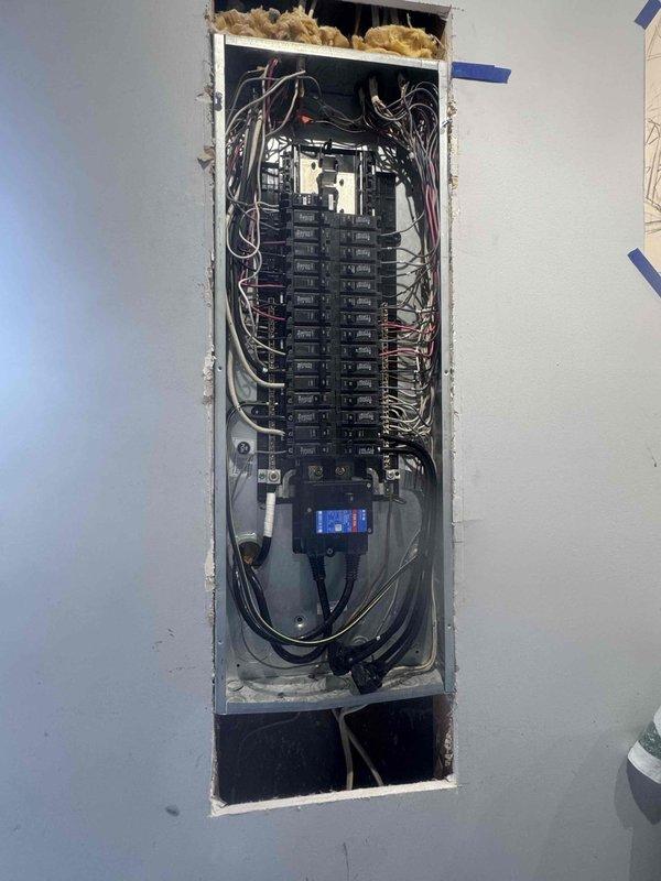 Responded to an install callback for a missing wire connection and a reported sewer odor at the water heater. Opened the drywall at the electrical panel, exposing the breaker box with the cover removed, to access and add the required wiring at the panel. Water heater odor complaint was documented for follow-up evaluation, including drain trap and venting inspection.