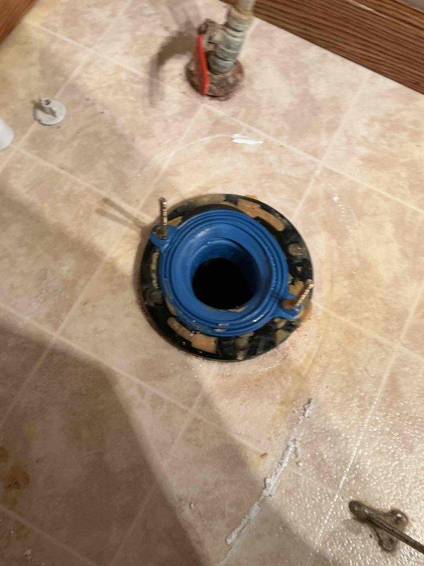 Responded to a leaking newly installed toilet, removed the unit, and inspected the closet flange, which showed rust staining, old wax and caulk residue, and moisture around the base. Cleaned the flange and surrounding floor, then reset the toilet with a new wax ring and closet bolts to restore a watertight seal at the drain connection.