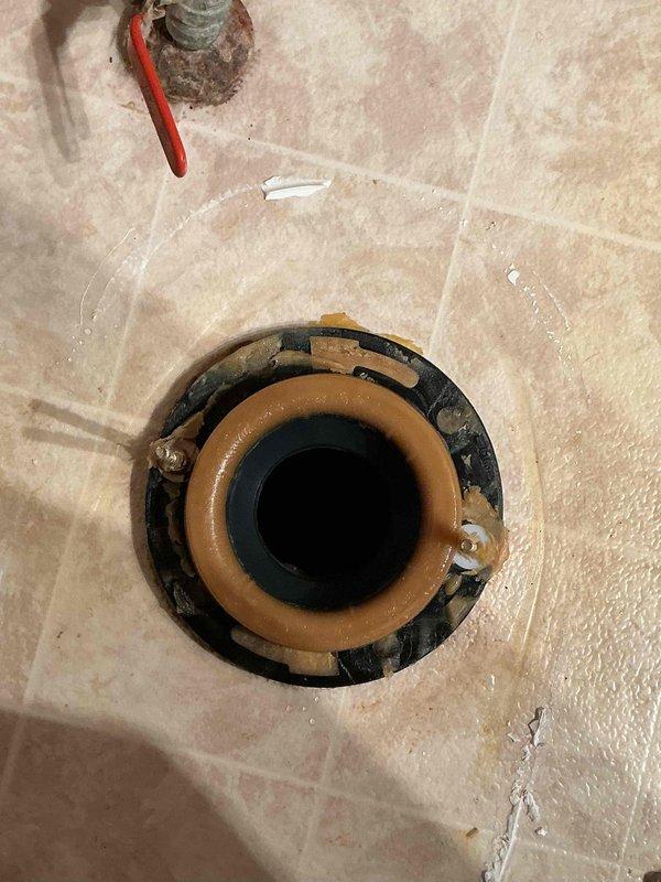 Responded to a leaking newly installed toilet, removed the unit, and inspected the closet flange, which showed rust staining, old wax and caulk residue, and moisture around the base. Cleaned the flange and surrounding floor, then reset the toilet with a new wax ring and closet bolts to restore a watertight seal at the drain connection.