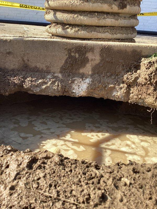 Responded to a leaking commercial main sewer line and excavated the affected section adjacent to the building, establishing a cordoned safety perimeter with caution tape and traffic cones. Exposed the line and identified active leakage, evidenced by standing foamy water and mineral deposits beneath the concrete slab and stacked corrugated pipe sections. The main line was repaired to stop the leak.