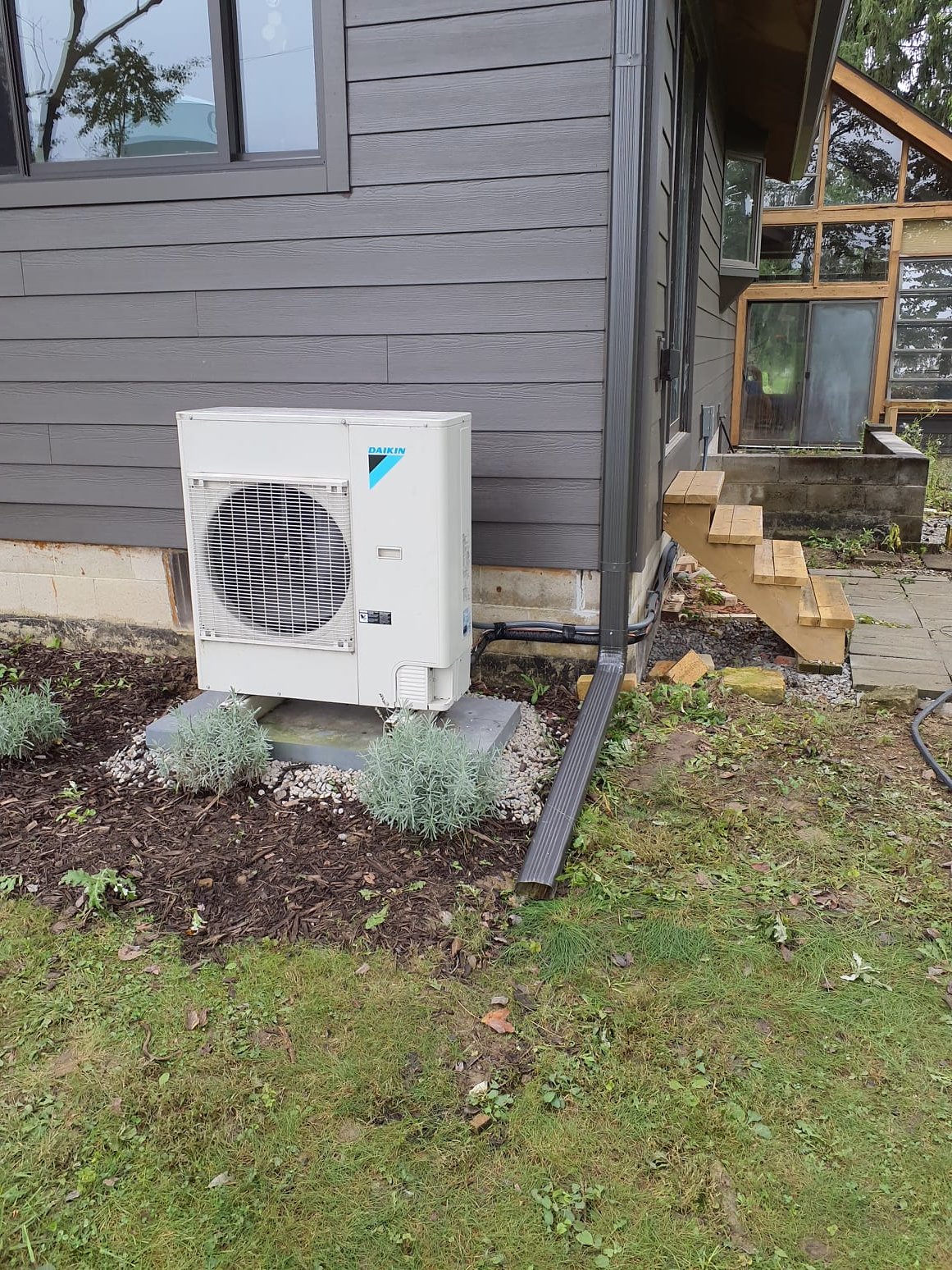 
Relocate existing air conditioner to new location left of back door stairs.
-Strap line set to foundation wall behind stairs
-Use gravel to build level spot for existing pad and rails
-Reuse existing electrical wire and disconnect

