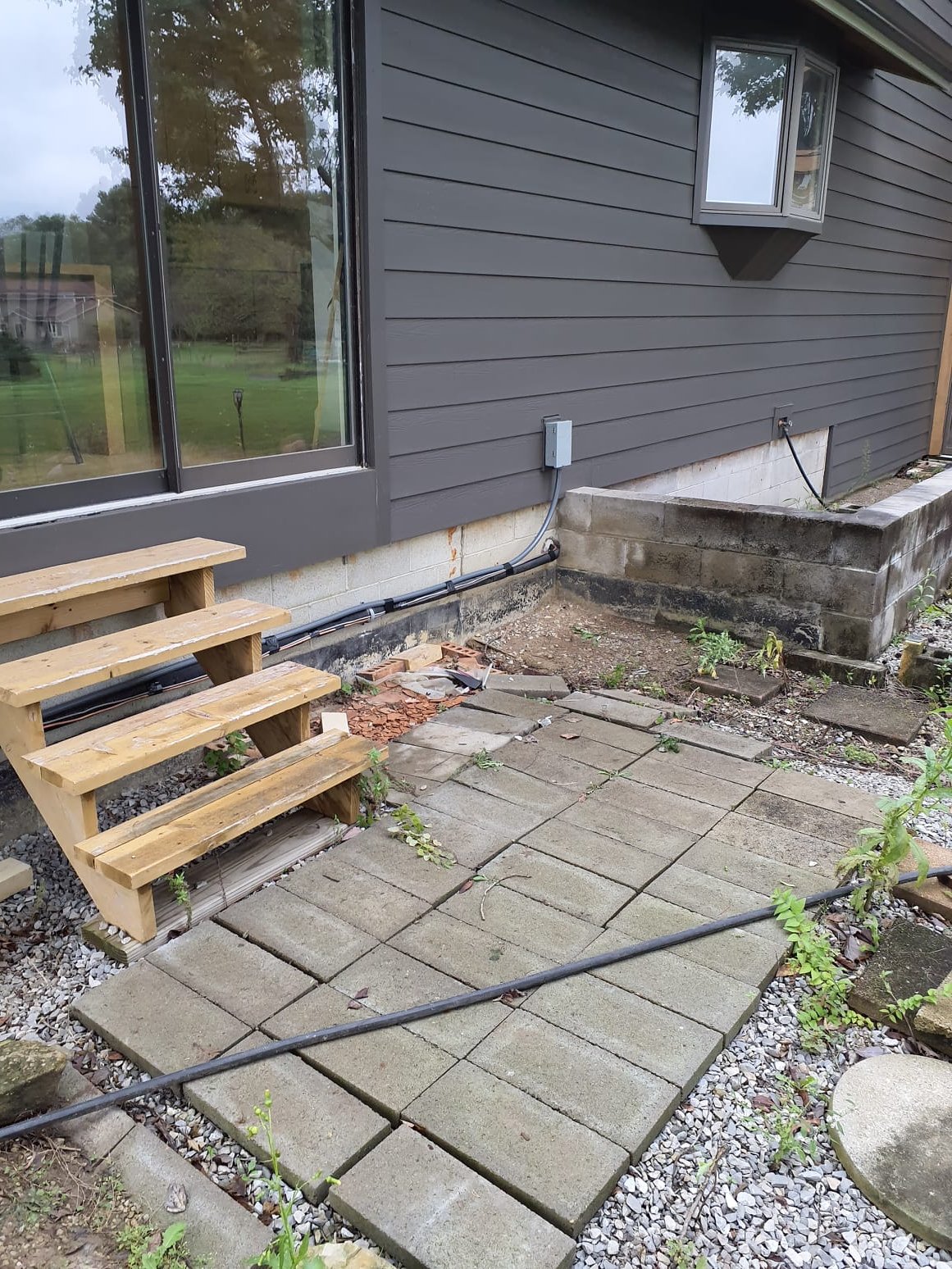 
Relocate existing air conditioner to new location left of back door stairs.
-Strap line set to foundation wall behind stairs
-Use gravel to build level spot for existing pad and rails
-Reuse existing electrical wire and disconnect

