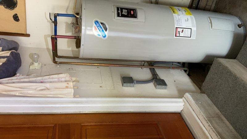 Inspected and documented a horizontally-mounted cylindrical water heater installation in a residential utility room. The unit displayed proper labeling, functional digital control panel, and appropriate copper piping connections with color-coded hot and cold water lines. Verified clearances and accessibility in the compact space shared with laundry appliances and confirmed the water heater was securely mounted on its platform support system.