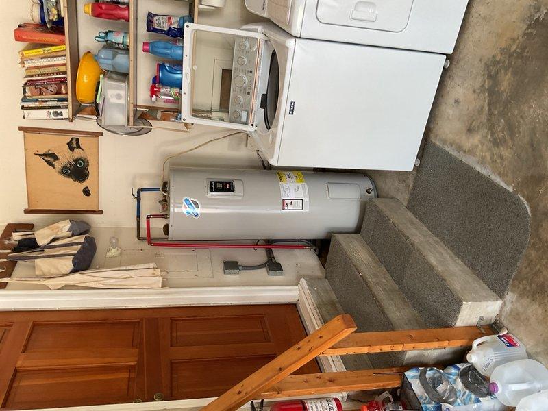 Inspected and documented a horizontally-mounted cylindrical water heater installation in a residential utility room. The unit displayed proper labeling, functional digital control panel, and appropriate copper piping connections with color-coded hot and cold water lines. Verified clearances and accessibility in the compact space shared with laundry appliances and confirmed the water heater was securely mounted on its platform support system.