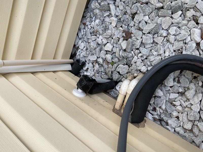 Installed outdoor water spigot system with Y-connector and dual hose setup on exterior wall with vinyl siding. Completed PVC drainage line installation at foundation level with proper gravel bed and landscape fabric for erosion control and weed prevention.