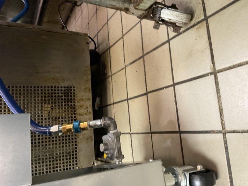 Performed inspection and documentation of gas water heater installation and associated plumbing connections in utility area. Verified proper installation of gas valve assembly, brass fittings, and blue flexible gas supply lines with appropriate safety labeling. Confirmed secure mounting of equipment, proper routing of black electrical conduit, and adequate clearances around unit. Documented condition of tile flooring in mechanical space and existing plumbing infrastructure for service records.