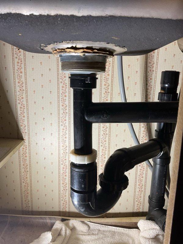 Responded to plumbing issue at residential kitchen sink. Upon inspection, identified deteriorated drain assembly with damaged sink material around the drain opening showing tears and discoloration. Assessed P-trap configuration and drain connections under sink cabinet. Verified water flow and drainage function with running water test to confirm system operation and check for potential leaks in the plumbing assembly.