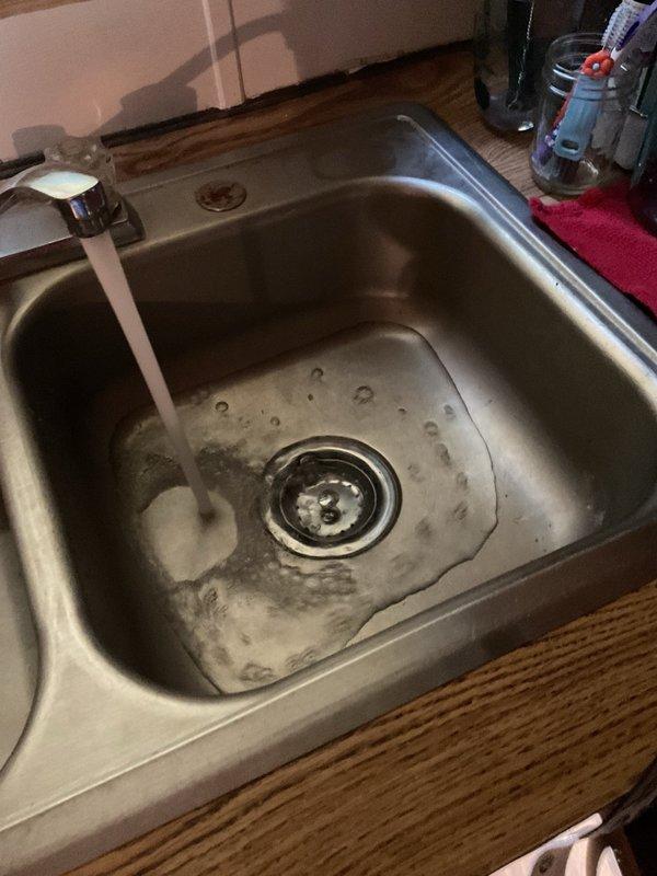 Responded to plumbing issue at residential kitchen sink. Upon inspection, identified deteriorated drain assembly with damaged sink material around the drain opening showing tears and discoloration. Assessed P-trap configuration and drain connections under sink cabinet. Verified water flow and drainage function with running water test to confirm system operation and check for potential leaks in the plumbing assembly.