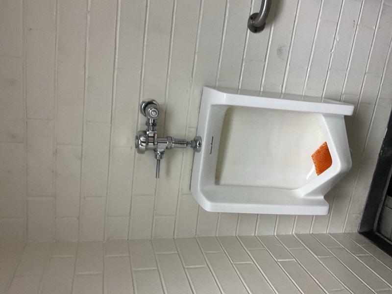 Responded to service call for utility sink inspection and documentation. Upon arrival, assessed the condition of the white porcelain utility sink with chrome faucet assembly and exposed plumbing connections. Photographed the installation showing the wall-mounted fixture with service-style faucet and visible shut-off valves. Documented the surrounding white beadboard paneling and tile flooring. Also photographed floor conditions in the service area, noting a small metal ring and general wear patterns on the light-colored tile surface. Completed visual inspection and photographic documentation of both the plumbing fixture and adjacent floor area for service records.