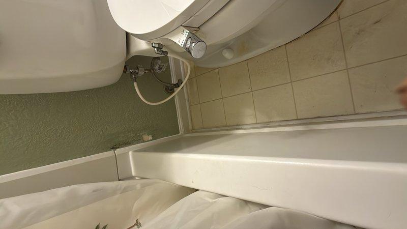 Completed photographic documentation of residential plumbing fixtures and laundry area. Captured bathroom installation showing standard white porcelain fixtures including bathtub with chrome faucet assembly and toilet with visible supply line connection. Documented existing tile conditions with beige ceramic floor and wall surfaces, noting visible staining on grout lines requiring attention. Also photographed laundry utility space showing wooden cabinetry, white appliances, and ceramic tile surfaces with textured wall finish in adjacent areas.