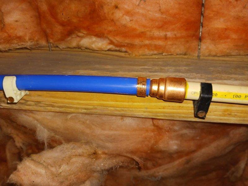Completed installation and routing of new PEX water supply line in attic crawl space, properly securing blue PEX piping alongside existing CSST gas line with appropriate mounting clips and support brackets to wooden joists. Ensured proper clearance between water and gas lines per code requirements, with all connections made using brass compression fittings and pipes supported against exposed fiberglass insulation.