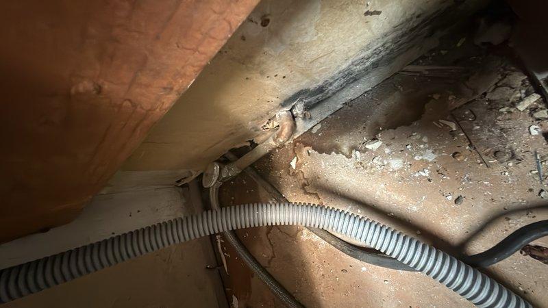 Inspected and documented plumbing infrastructure in confined crawl space beneath residential structure. Verified proper installation and operational status of drainage system components, including metal trap assembly and flexible ductwork secured to wooden framing members. Assessed condition of exposed plumbing fixtures and confirmed all connections were intact and functioning within normal parameters.