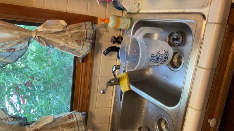 Completed installation of stainless steel double-basin kitchen sink with modern curved faucet assembly featuring dual-handle controls and brushed metallic finish. All fixtures properly mounted in tiled countertop with secure connections and verified drainage functionality in both basins.