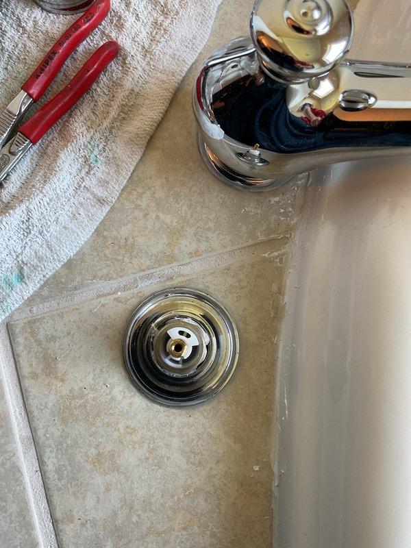 Completed plumbing repair work on bathroom fixtures including bathtub faucet valve assembly replacement and sink drain service. Addressed water flow issues by accessing and replacing the brass valve cartridge behind the tub faucet escutcheon plate, and cleared mineral deposits and buildup from the bathroom sink basin and chrome drain assembly to restore proper drainage function.